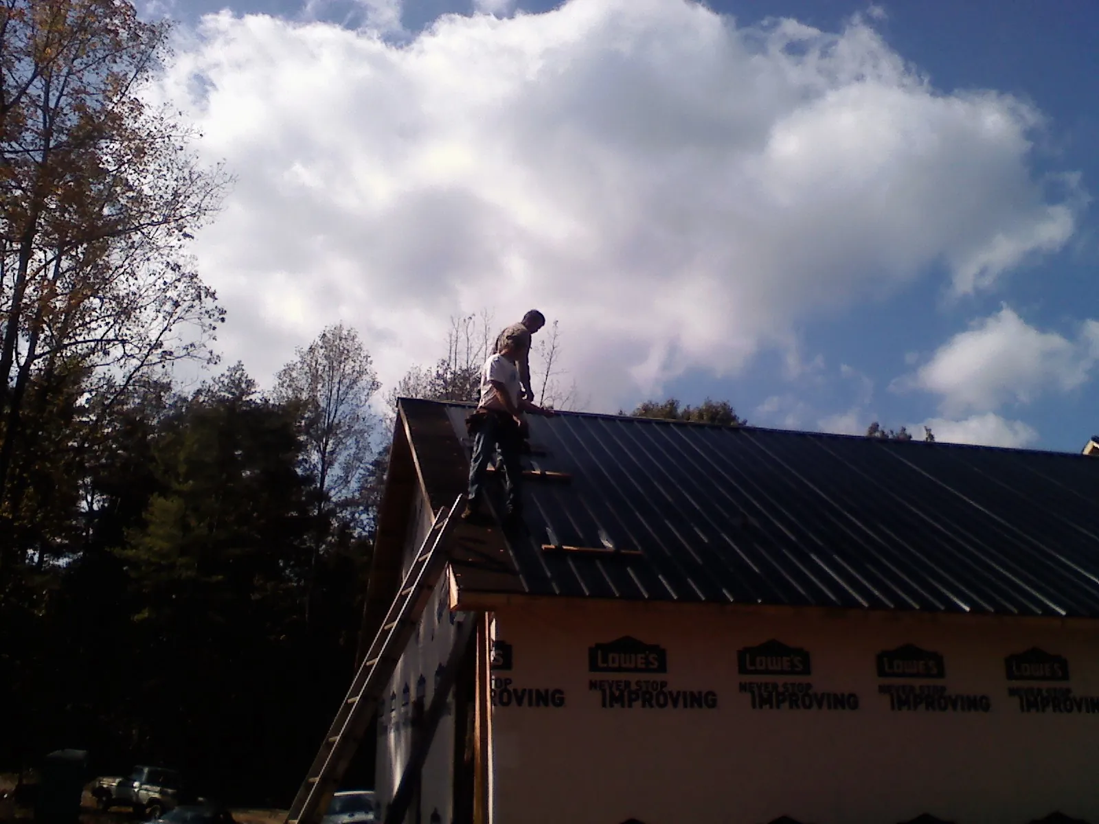 Roofer fastening dark metal panels high against a cloudy sky, from a Roof Inspection job in Elberta